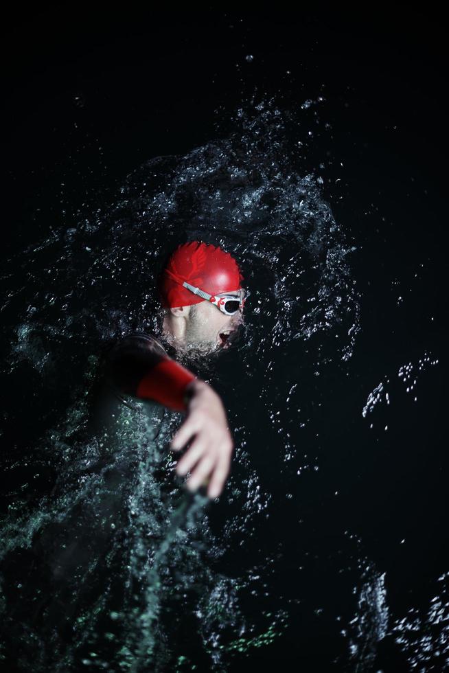 atleta de triatlón real nadando en la noche oscura foto