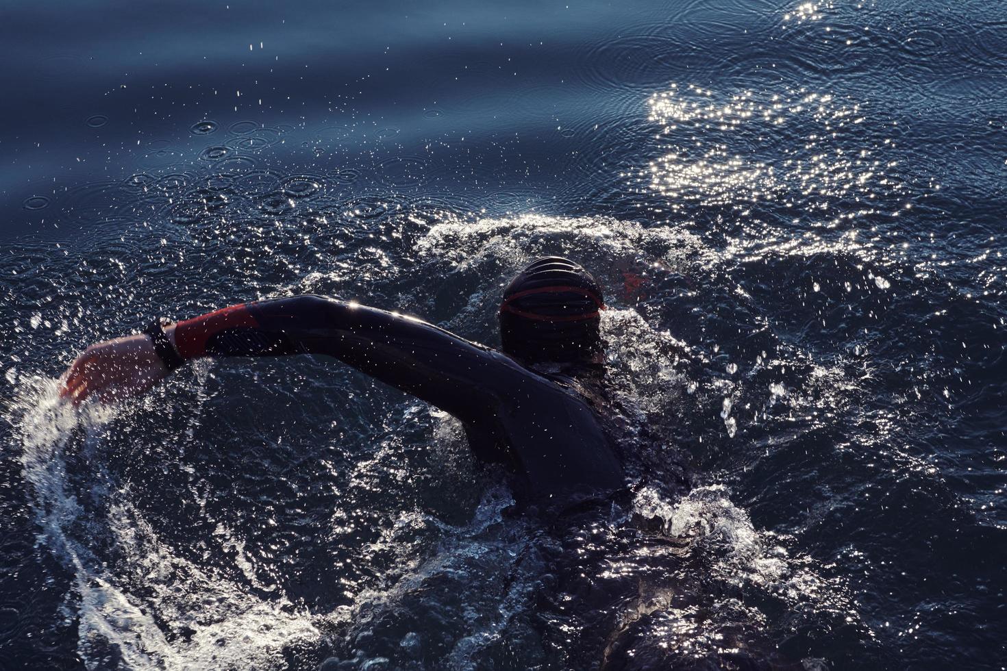 triathlon athlete swimming on lake in sunrise  wearing wetsuit photo