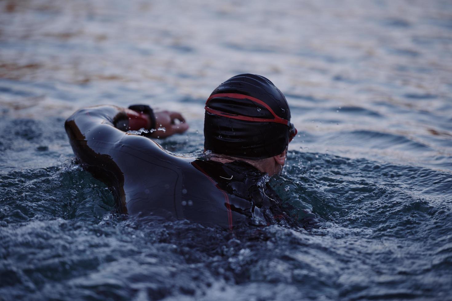 atleta de triatlón nadando en el lago al amanecer usando traje de neopreno foto