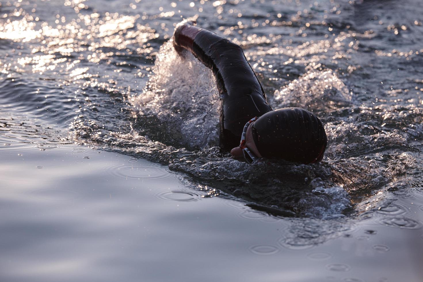 atleta de triatlón nadando en el lago al amanecer usando traje de neopreno foto