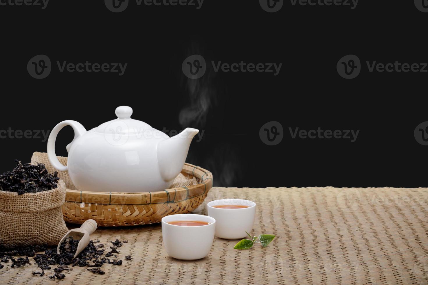 taza de té caliente con tetera, hojas de té verde y hierbas secas en la alfombra de bambú por la mañana aísle el fondo negro con espacio vacío, producto orgánico de la naturaleza para la salud con el tradicional foto