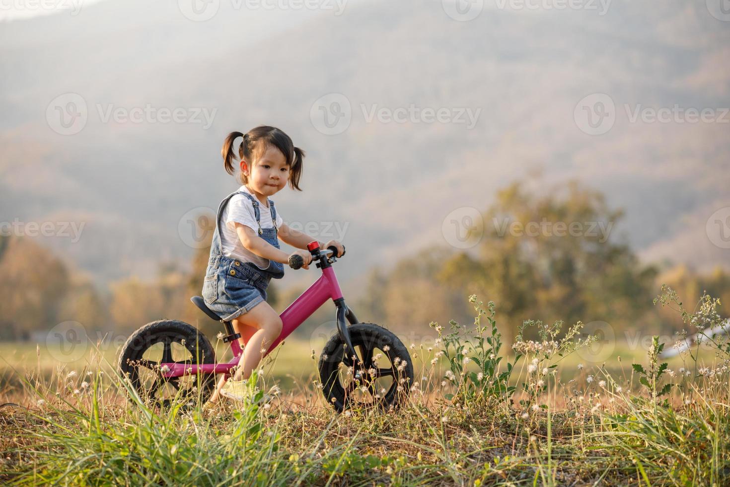 niño feliz montando en bicicleta. niña en una bicicleta rosa. Actividad de verano saludable para niños en edad preescolar. niños jugando afuera. niña aprende foto