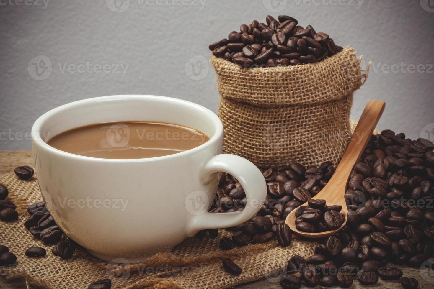 taza de café caliente con granos de café en la mesa de madera y el fondo negro, efecto de color de estilo vintage foto