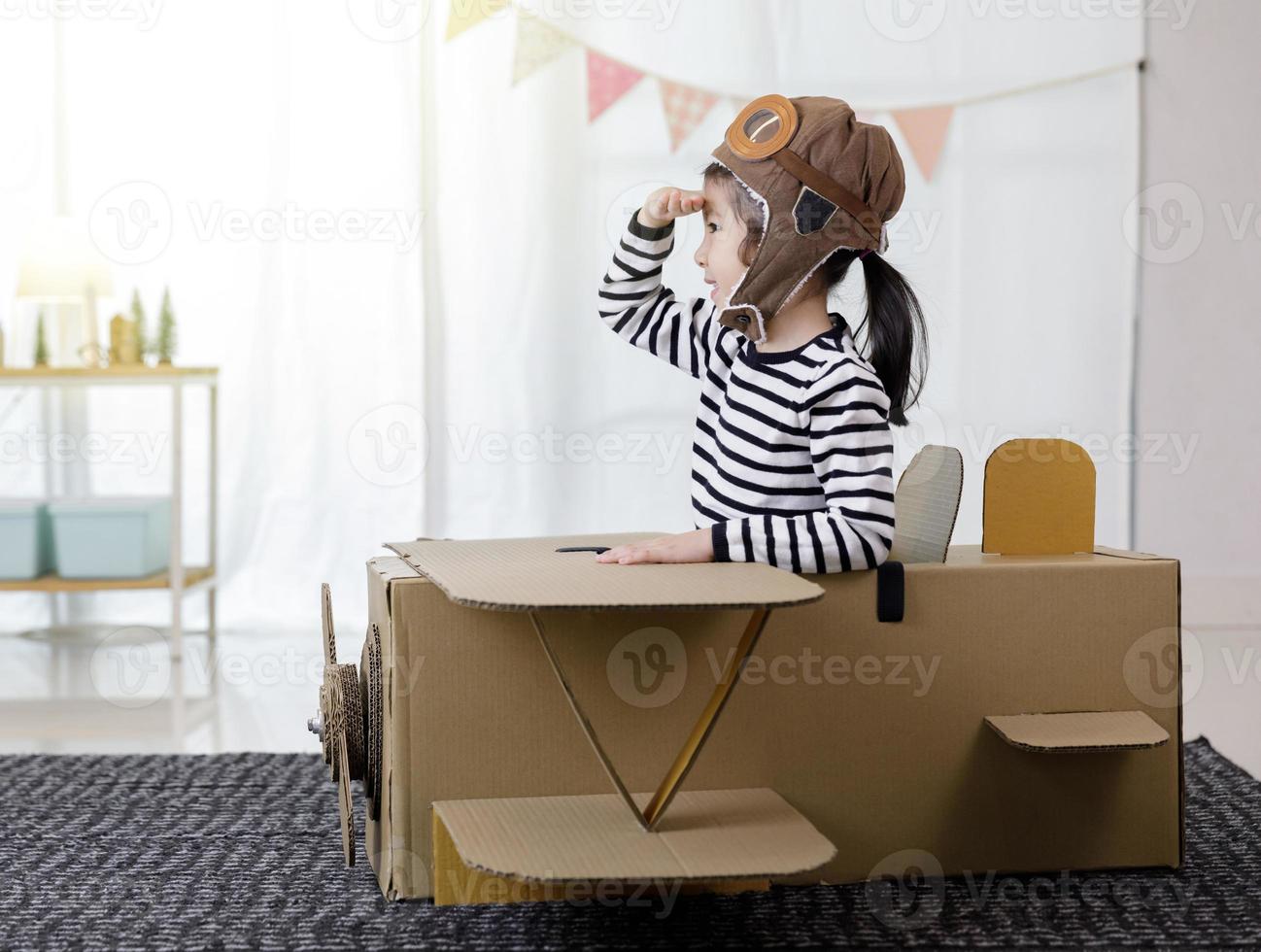 Niña asiática jugando con artesanía de avión de juguete de cartón aislada en casa con espacio de copia para su texto, creativa con la familia y soñando con el concepto de vuelo foto