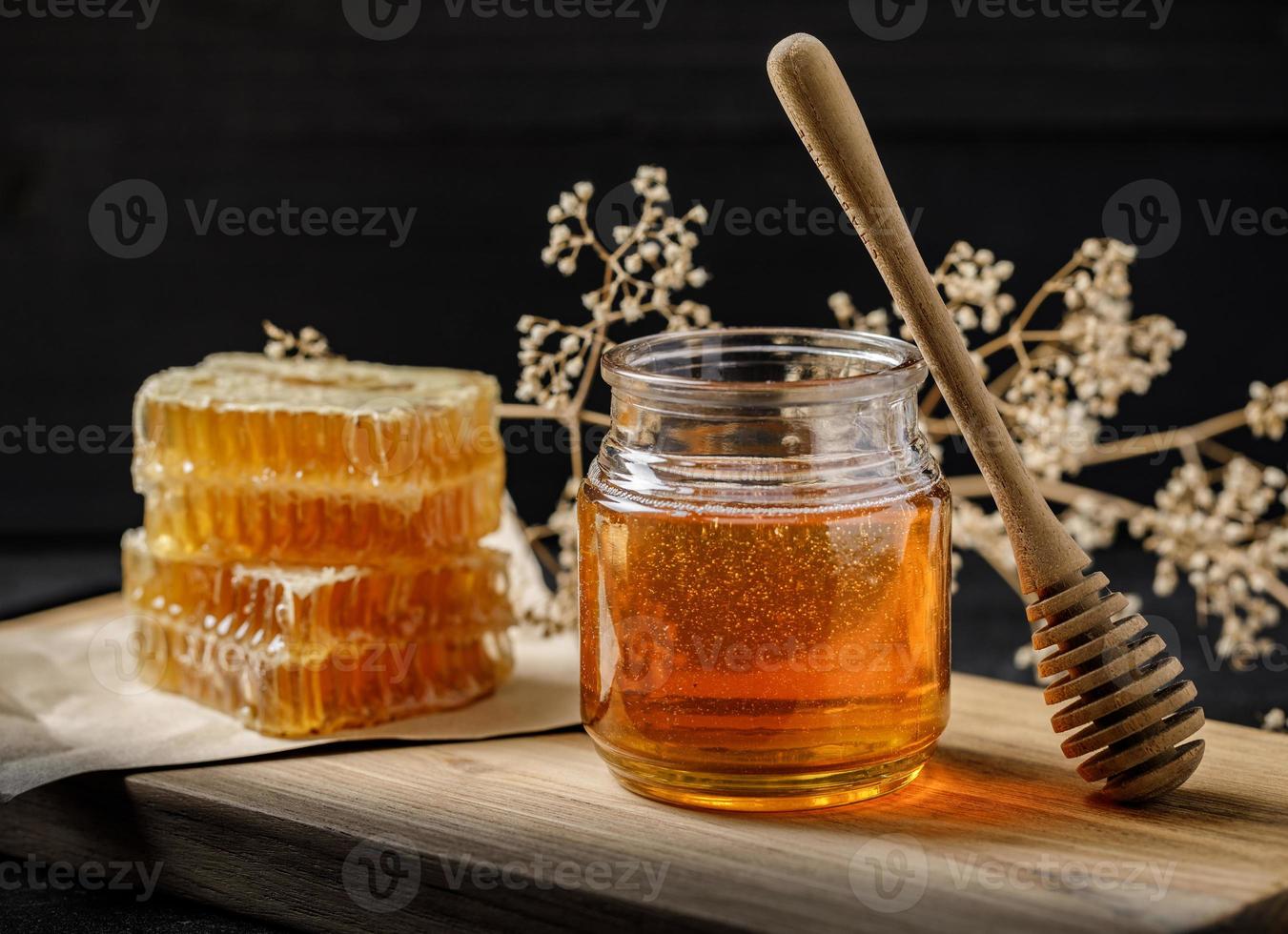 panal con cucharón de miel y flor seca sobre fondo negro, productos de abejas por concepto de ingredientes naturales orgánicos foto