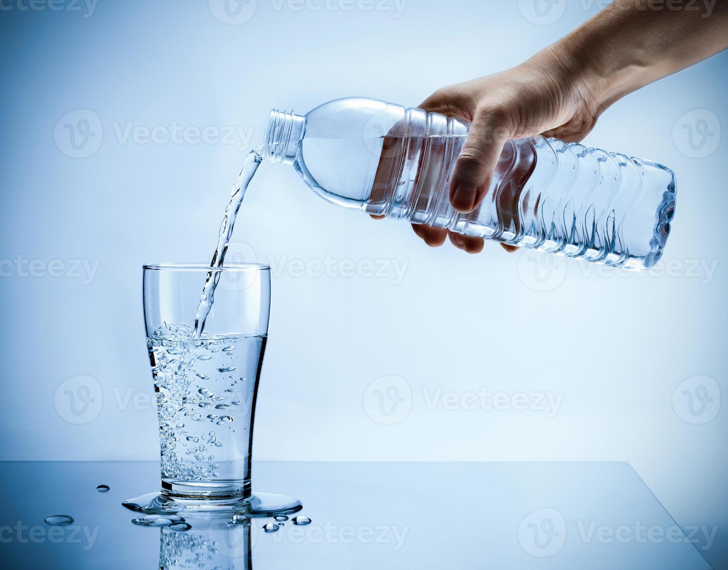 Hand pouring fresh pure water from bottle into a glass on the table