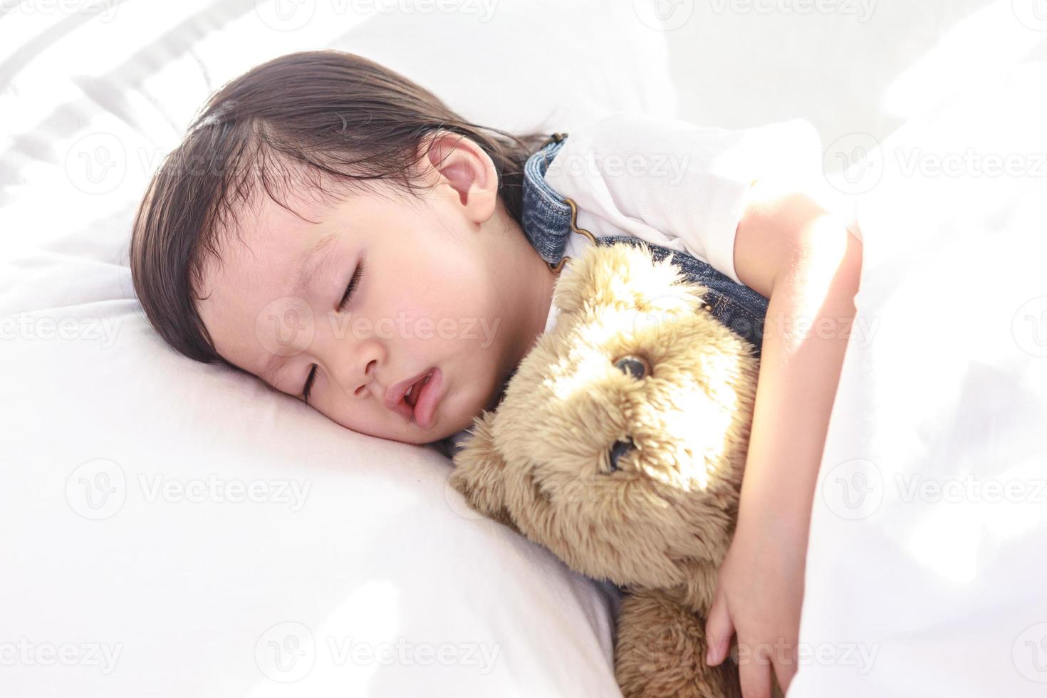 Little asian girl sleeping with her toy teddy bear photo
