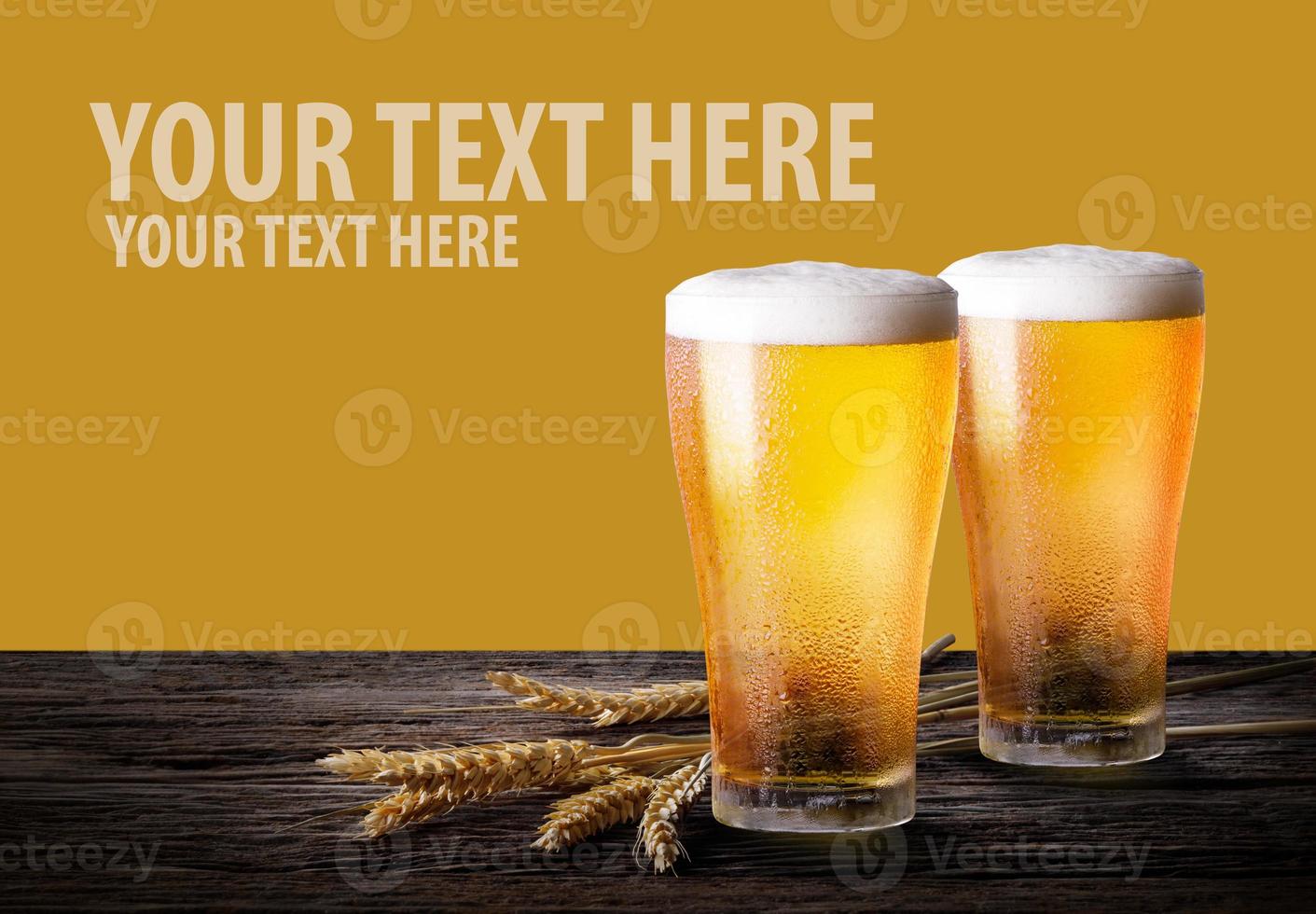 Cold beer with wheat on wooden table. Glasses of light beer on the yellow background with copy space. photo