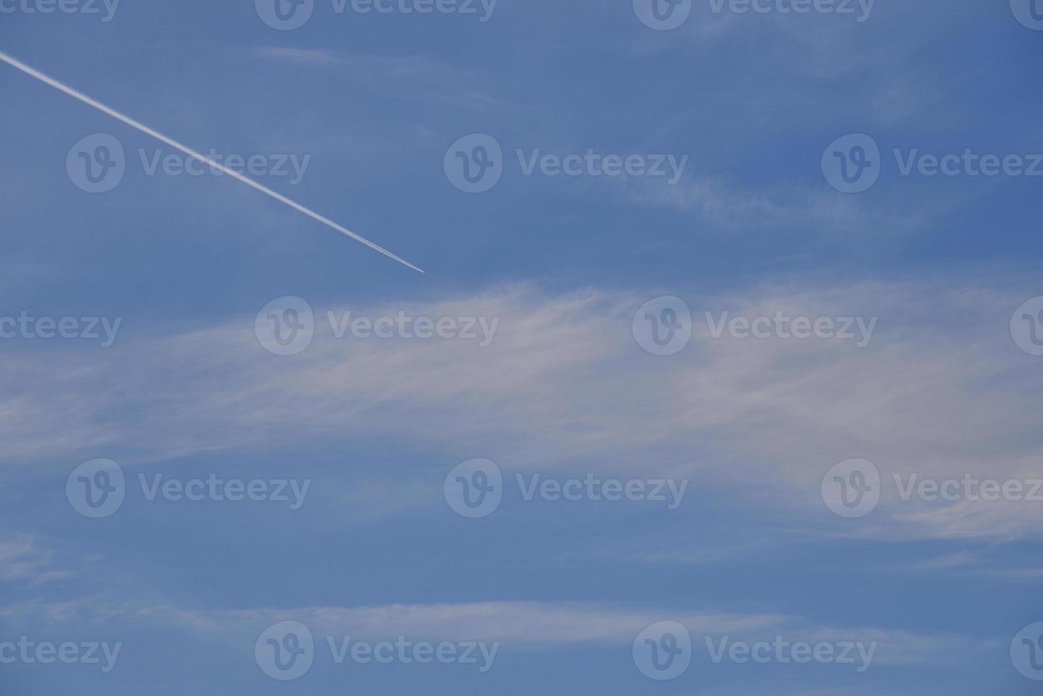 A plane flying in the blue sky and clouds. A white contrail from an airplane in the summer sky. photo