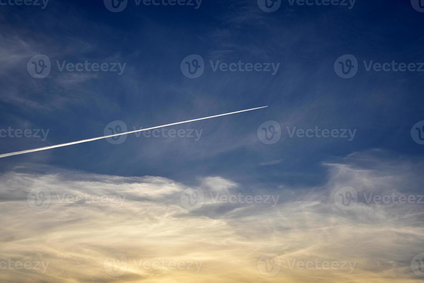 A plane flying in the blue sky and clouds. A white contrail from an airplane in the summer sky. photo