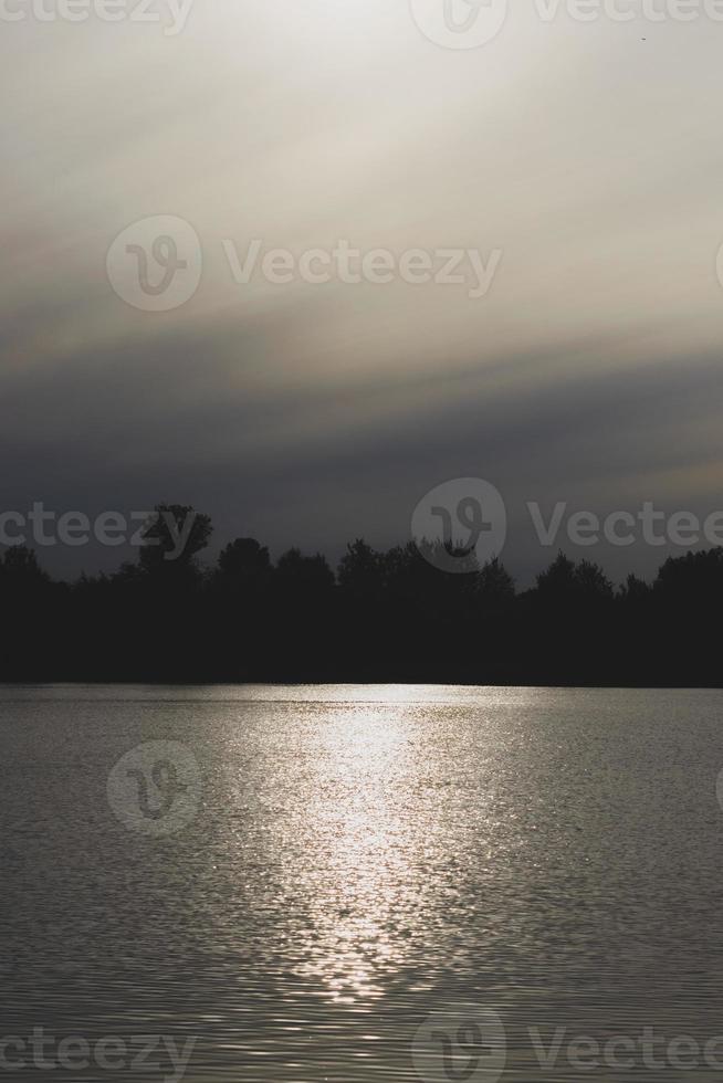 Atmospheric sunset behind trees and reflection in water. photo