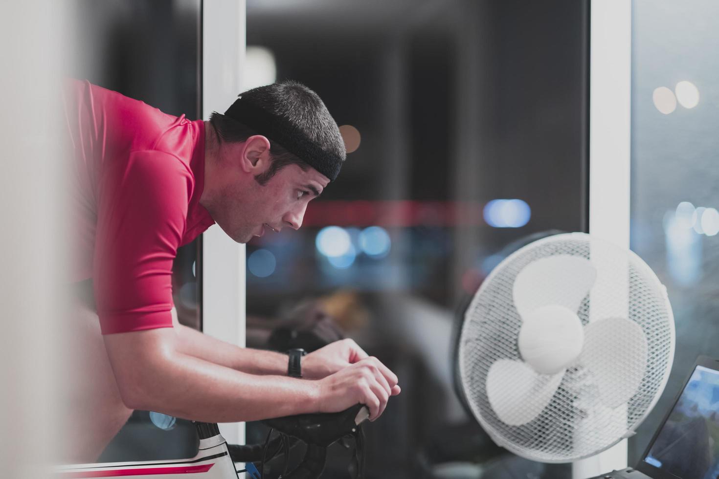 hombre en bicicleta en el entrenador de la máquina que está haciendo ejercicio en el hogar por la noche jugando al juego de carreras de bicicletas en línea foto