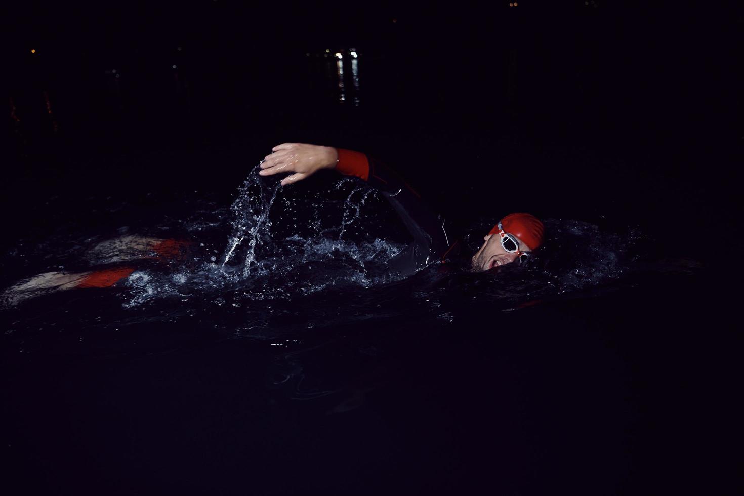 triathlon athlete swimming in dark night  wearing wetsuit photo