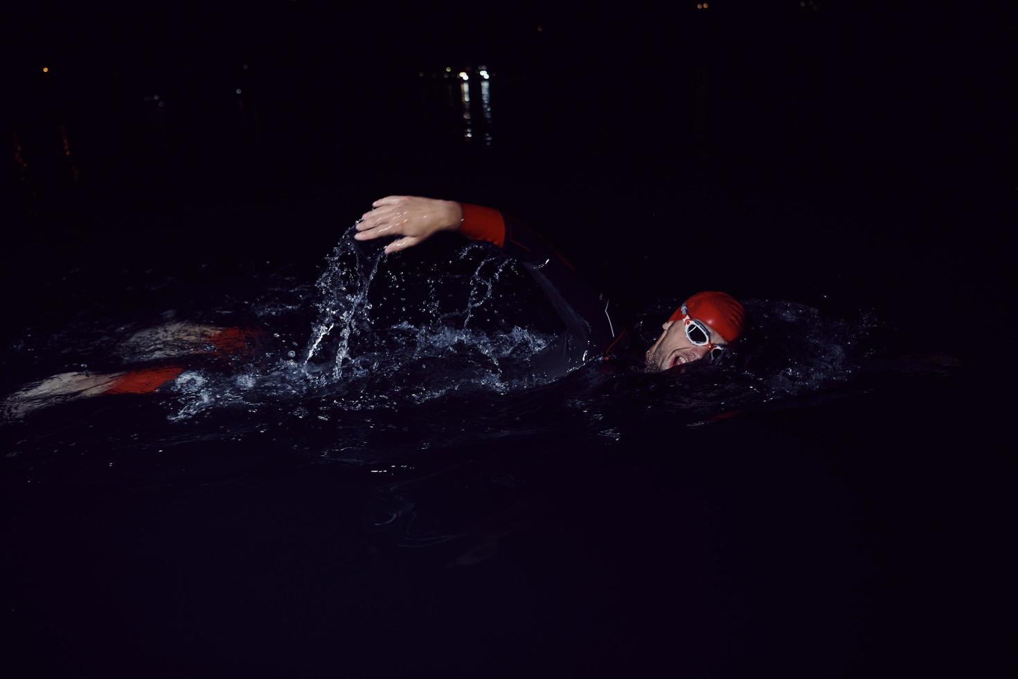 atleta de triatlón nadando en la noche oscura con traje de neopreno foto