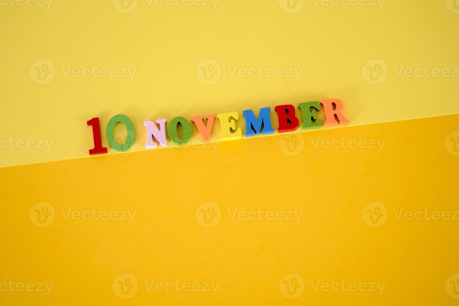 November 10 on a yellow, paper background with multicolored and wooden letters with space for text. photo