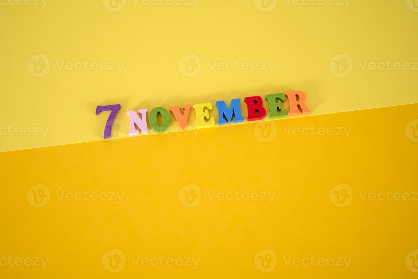 November 7 on a yellow, paper background with multicolored and wooden letters with space for text. photo