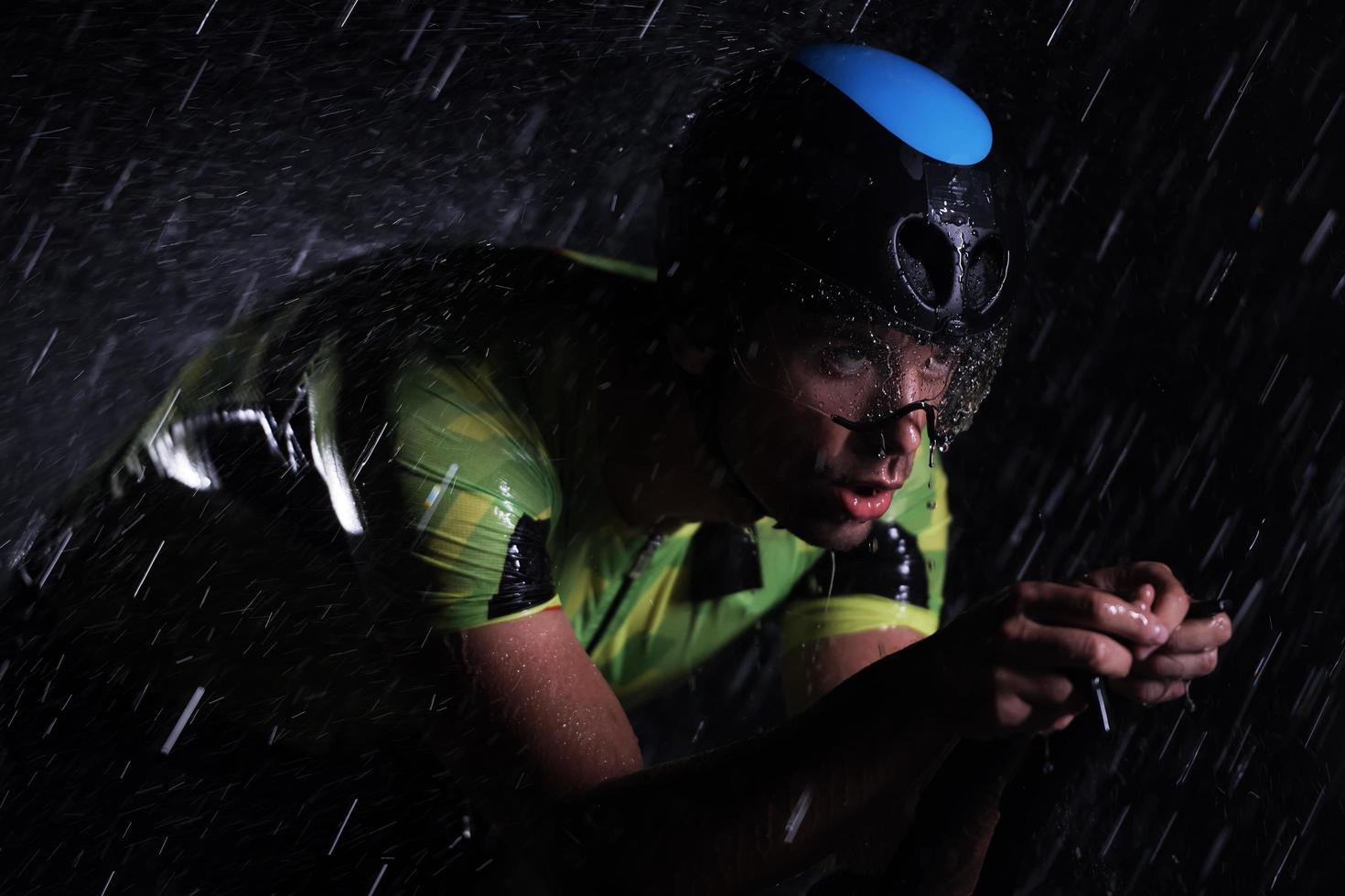 atleta de triatlón montando bicicleta rápido en una noche lluviosa foto