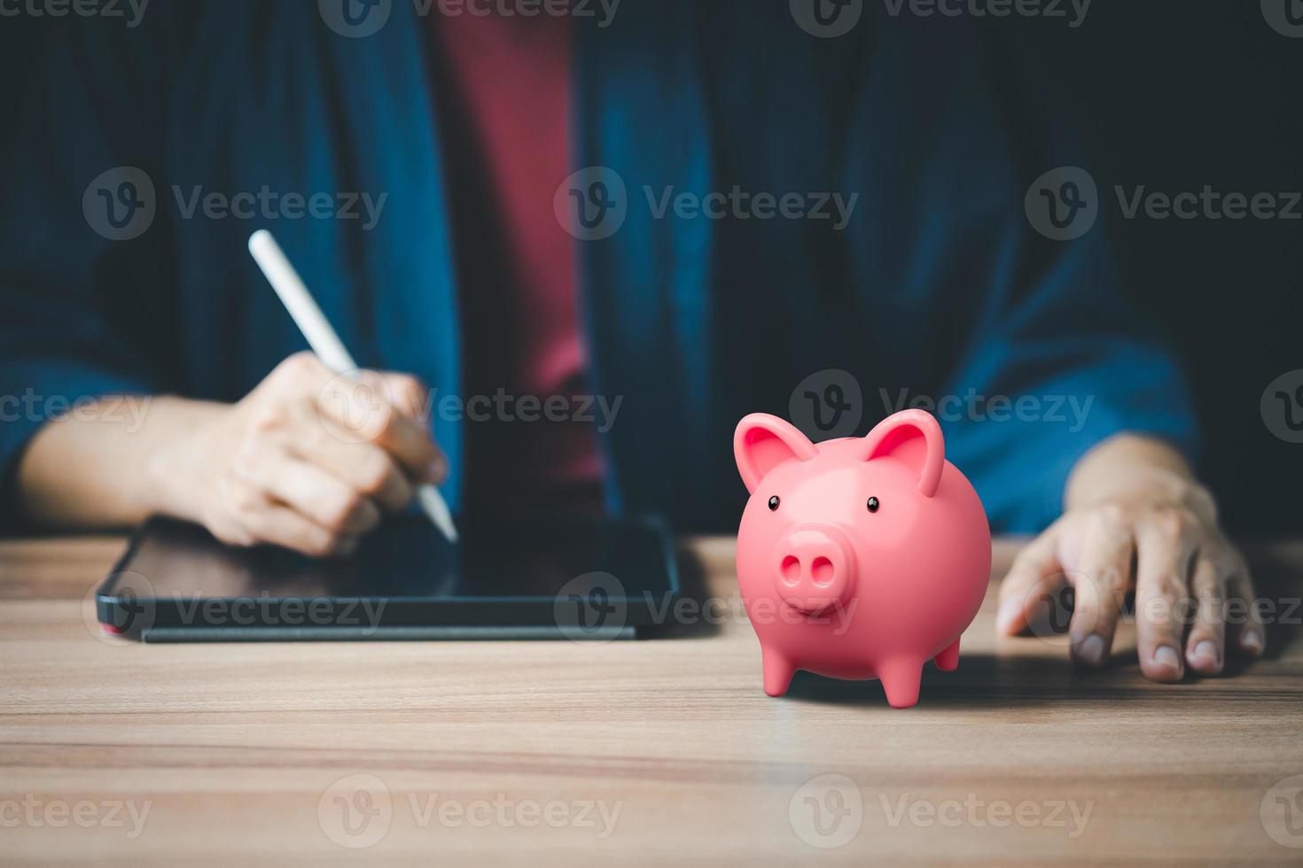 Closeup image of a pink piggy bank and taking note on the tablet for planning, saving money wealth and financial concept. Business online, finance and investment. photo