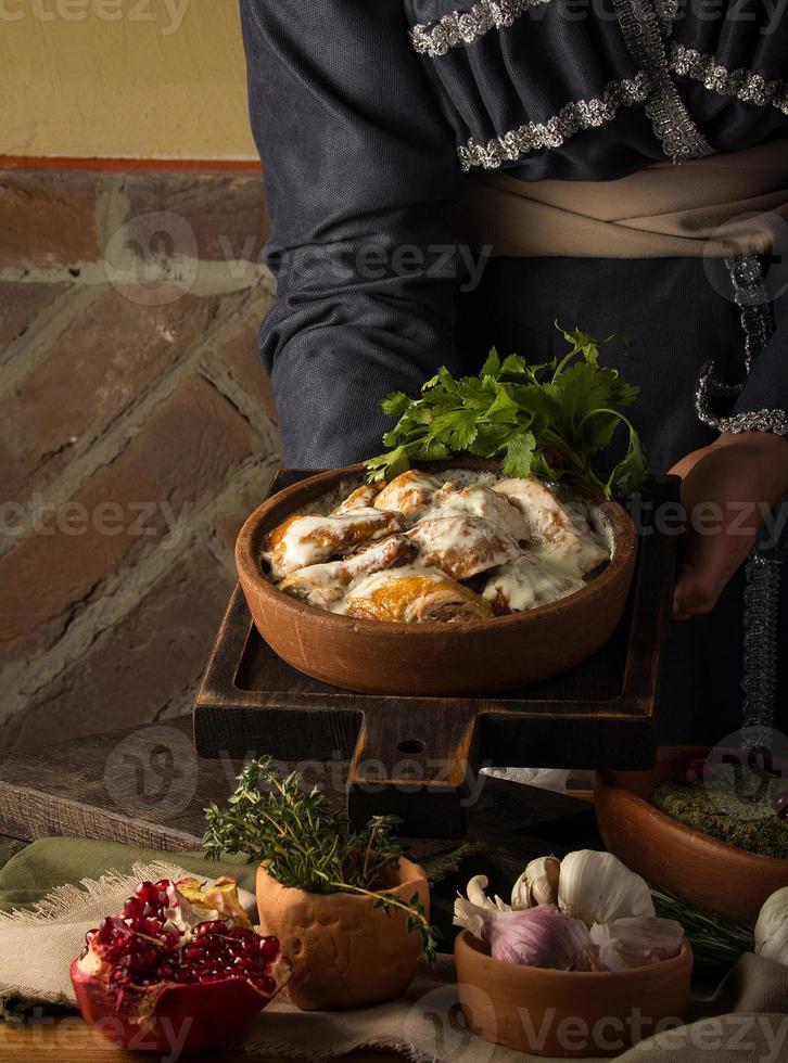 A vertical shot of a waitress presenting a chicken covered in a creamy sauce photo