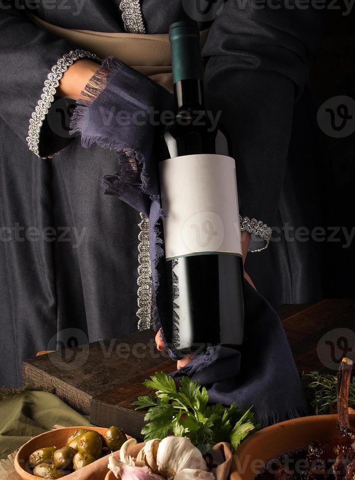 A vertical shot of a person in a traditional costume showing a wine bottle photo