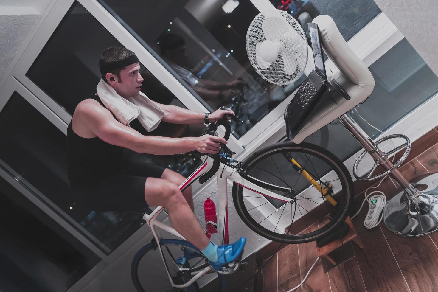 hombre en bicicleta en el entrenador de la máquina que está haciendo ejercicio en el hogar por la noche jugando al juego de carreras de bicicletas en línea foto