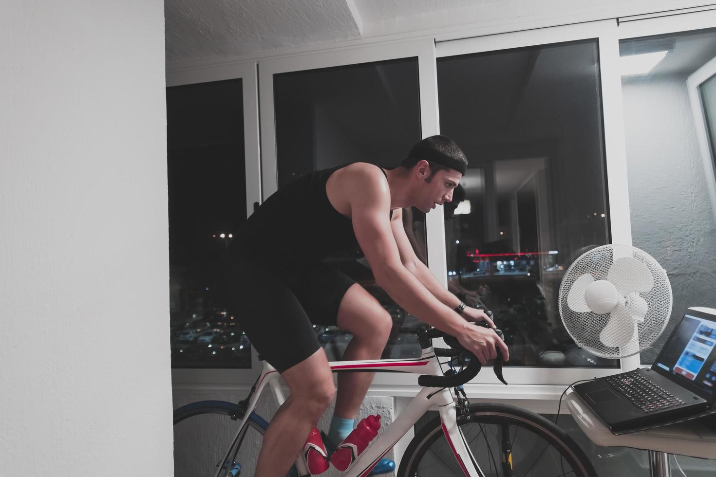 Man cycling on the machine trainer he is exercising in the home at night playing online bike racing game photo