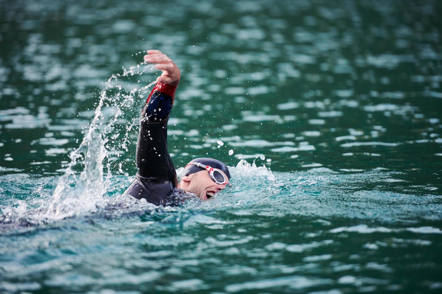 triathlon athlete swimming on lake in sunrise  wearing wetsuit photo