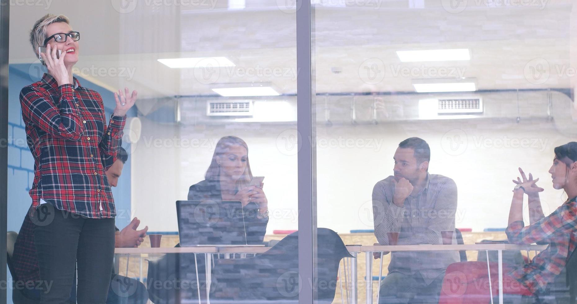 Business Woman Looking Through A Window And using On A Cell Phone during bussines meeting photo
