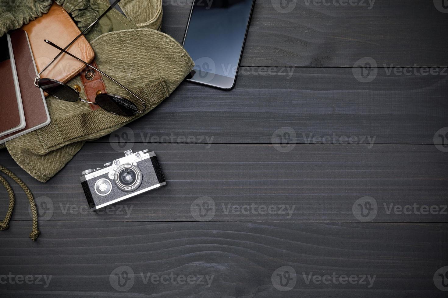 Top view mockup of Traveler's accessories with passport, mobile phone, wallet, camera, hat amd backpack on black wooden desk empty space, Travel concept background photo