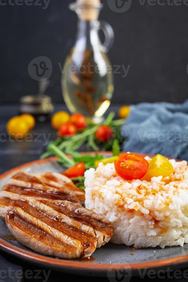 Rice with grilled pork meat, tomatoes and green herbs on dark background photo