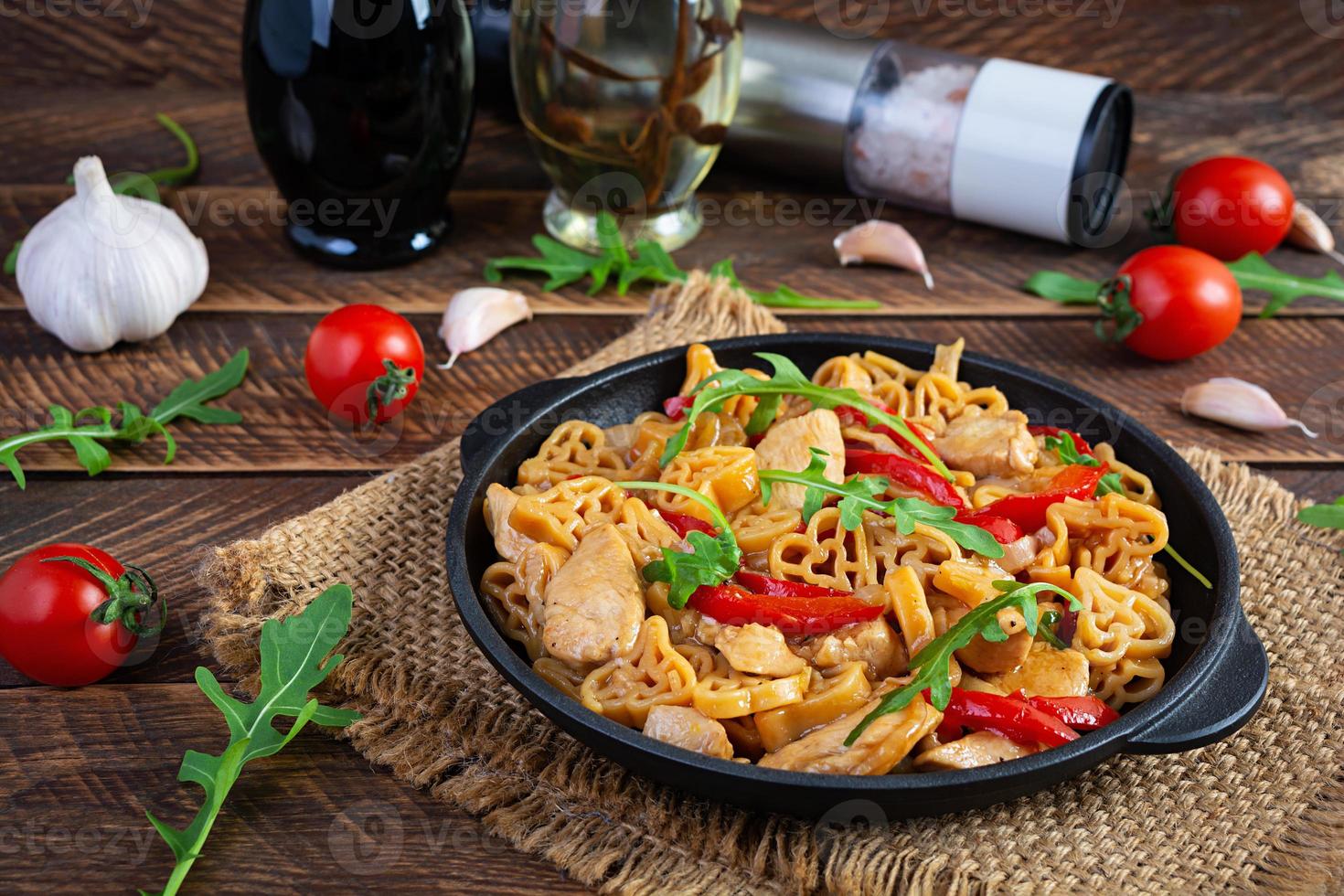 Tasty pasta in tomato sauce with chicken, pepper and herbs on wooden background photo