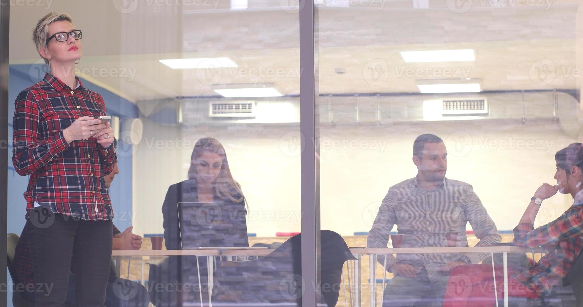 Business Woman Looking Through A Window And using On A Cell Phone during bussines meeting photo