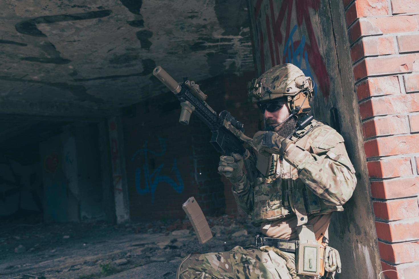 A bearded soldier in special forces uniform in dangerous military mission, refile his weapon while hiding from the wall. Selective focus photo