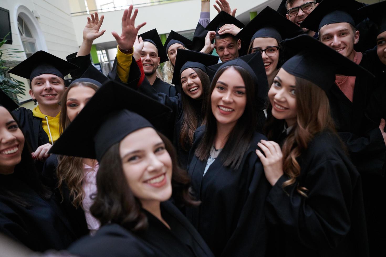 group of happy international students in mortar boards and bachelor gowns with diplomas taking selfie by smartphone photo