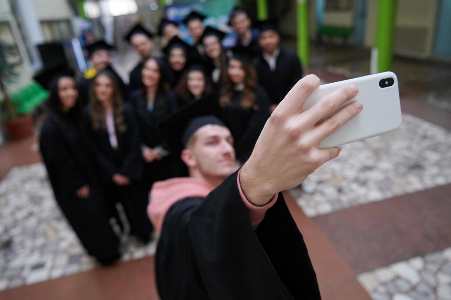 group of happy international students in mortar boards and bachelor gowns with diplomas taking selfie by smartphone photo