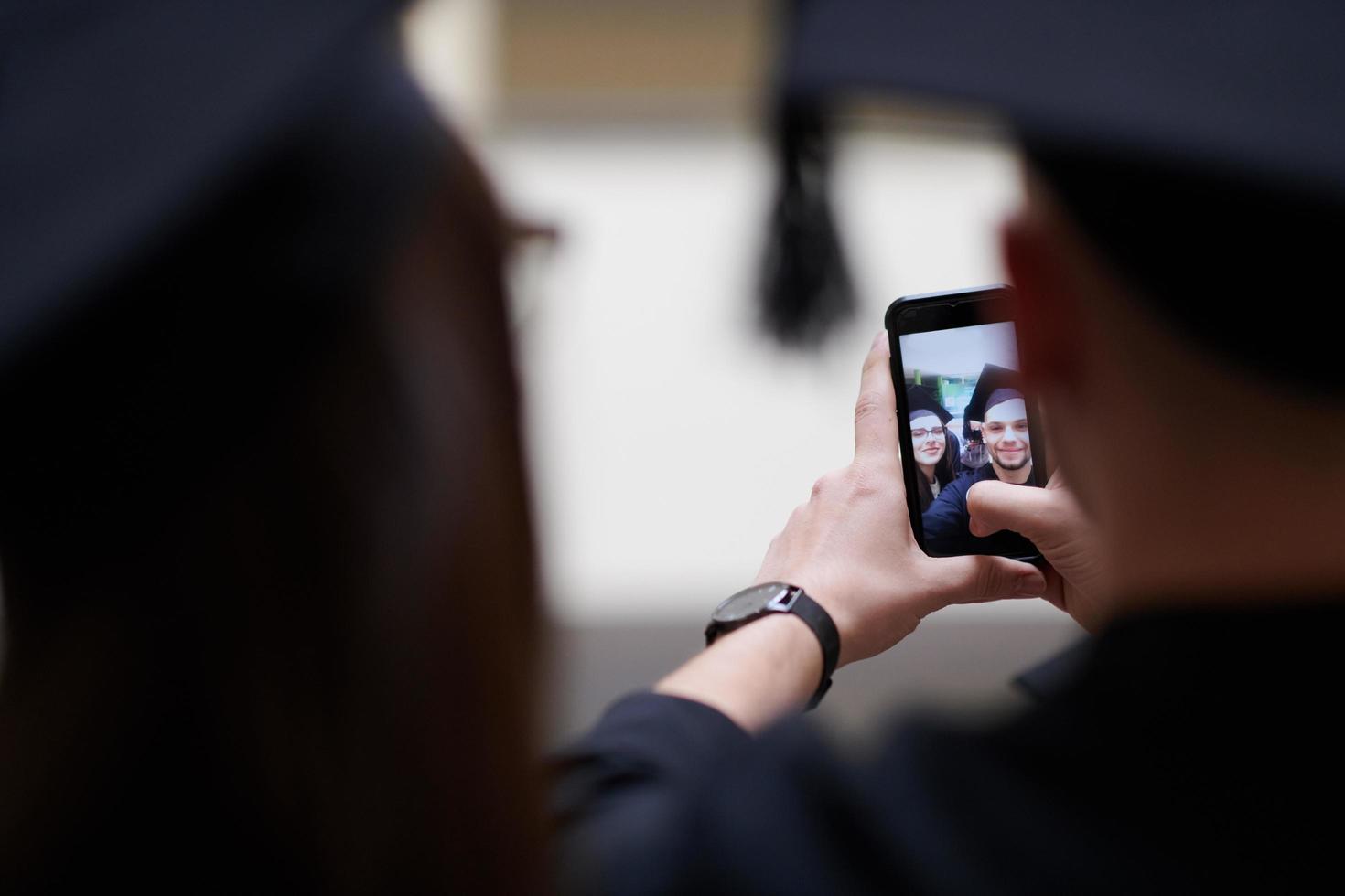 grupo de estudiantes internacionales felices en juntas de mortero y batas de soltero con diplomas tomando selfie por teléfono inteligente foto