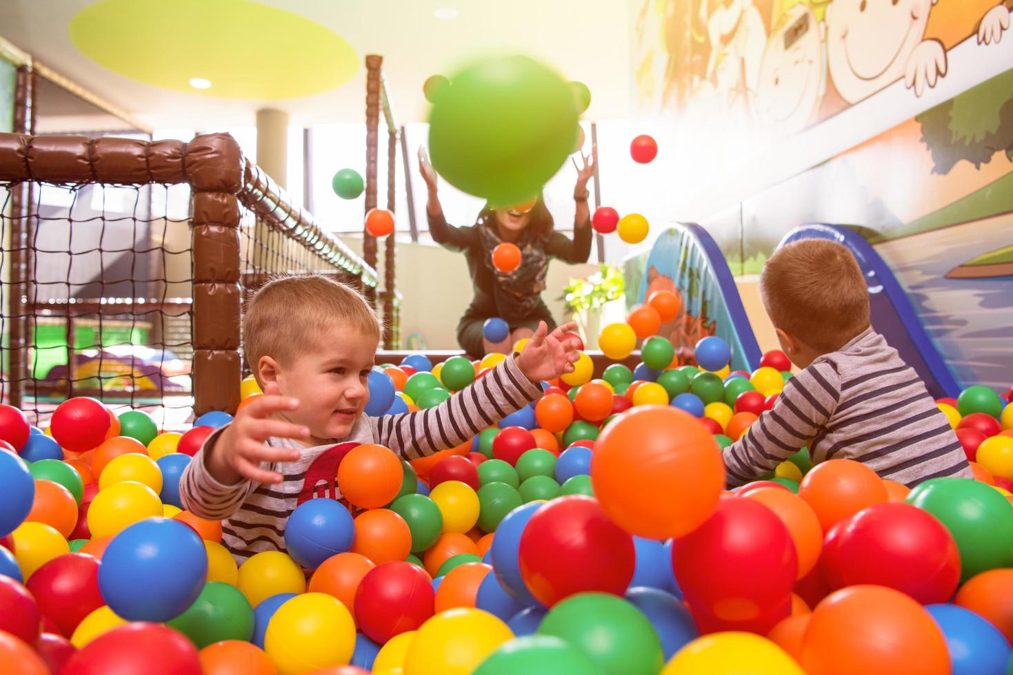 young mom playing with kids in pool with colorful balls photo