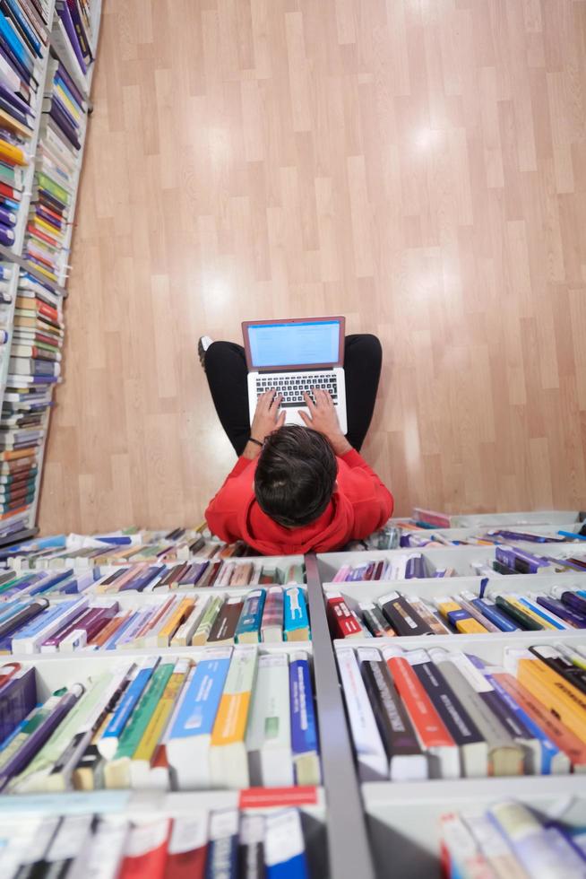image of someone sitting on the ground with a laptop in the library book stacks