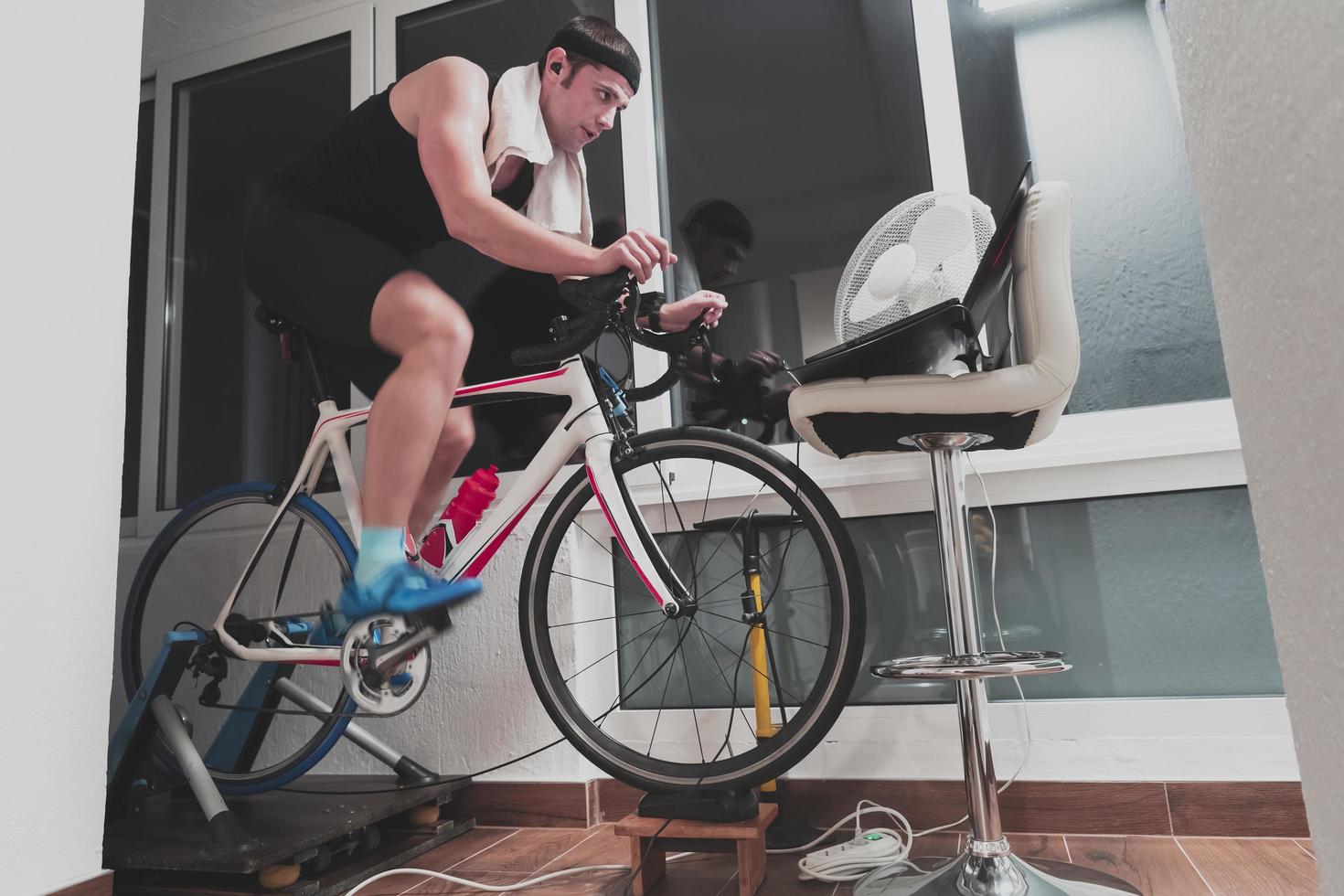 hombre en bicicleta en el entrenador de la máquina que está haciendo ejercicio en el hogar por la noche jugando al juego de carreras de bicicletas en línea foto