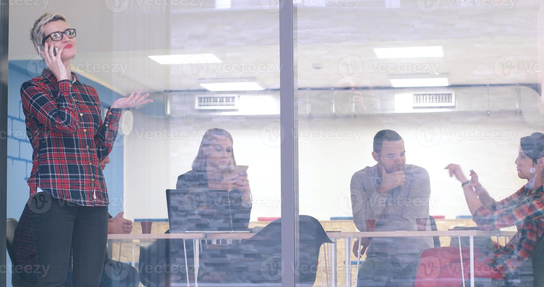 Business Woman Looking Through A Window And using On A Cell Phone during bussines meeting photo