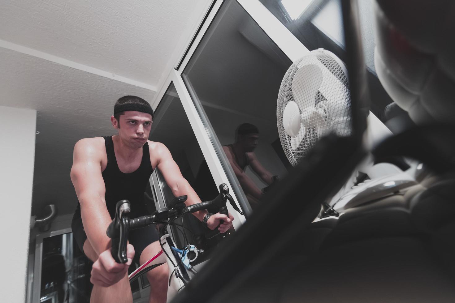 hombre en bicicleta en el entrenador de la máquina que está haciendo ejercicio en el hogar por la noche jugando al juego de carreras de bicicletas en línea foto