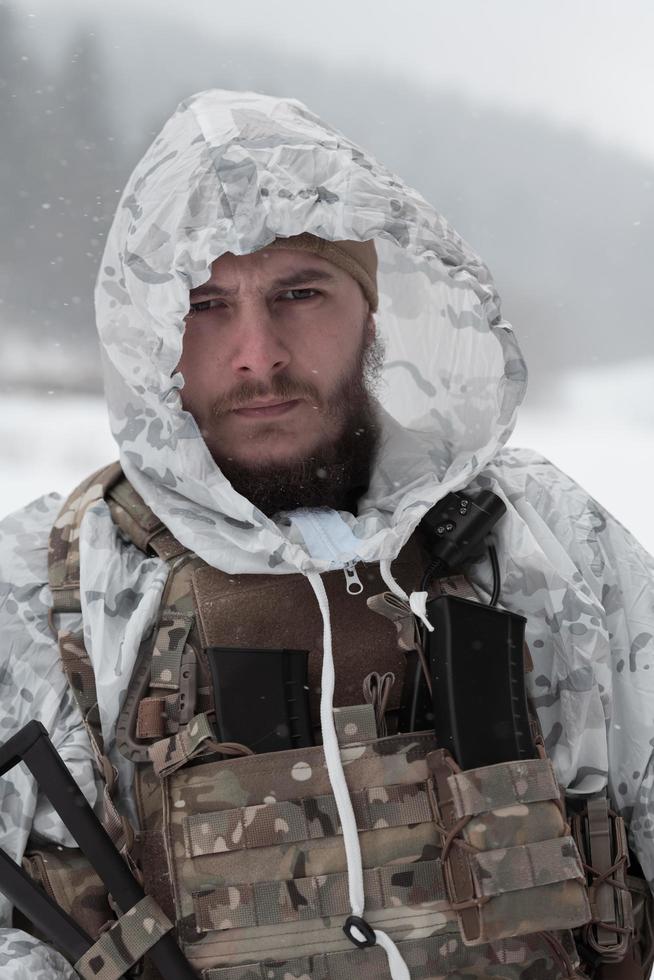 Winter war in the Arctic mountains. Operation in cold conditions.Soldier in winter camouflaged uniform in Modern warfare army on a snow day on forest battlefield with a rifle. Selective focus photo