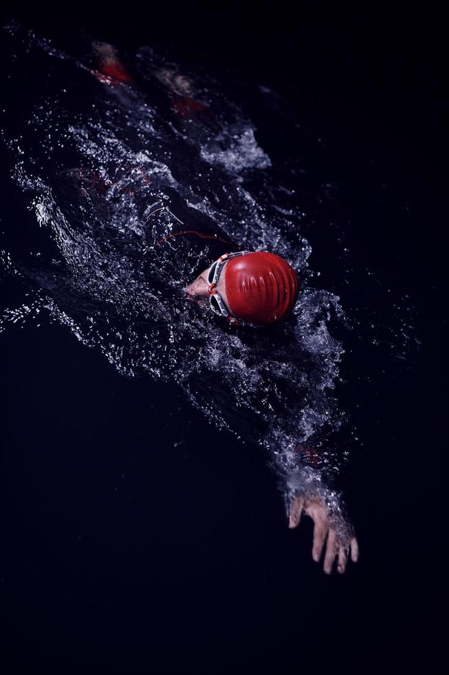 triathlon athlete swimming in dark night  wearing wetsuit photo