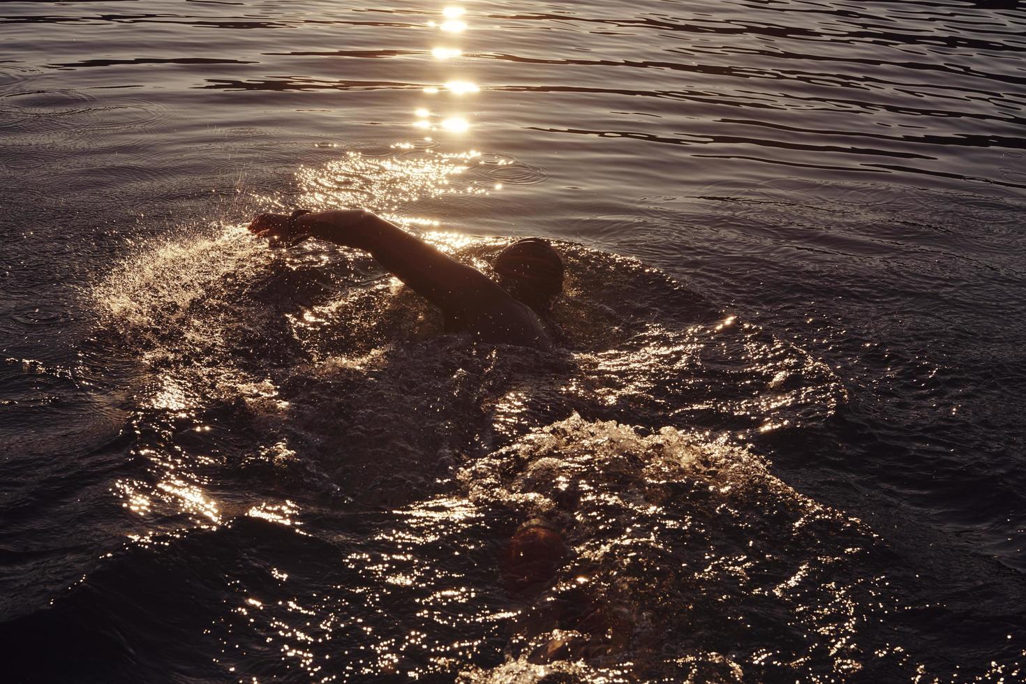 triathlon athlete swimming on lake in sunrise  wearing wetsuit photo