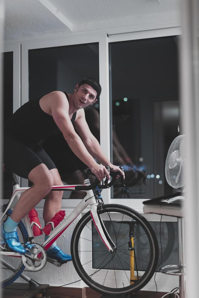 Man cycling on the machine trainer he is exercising in the home at night playing online bike racing game photo