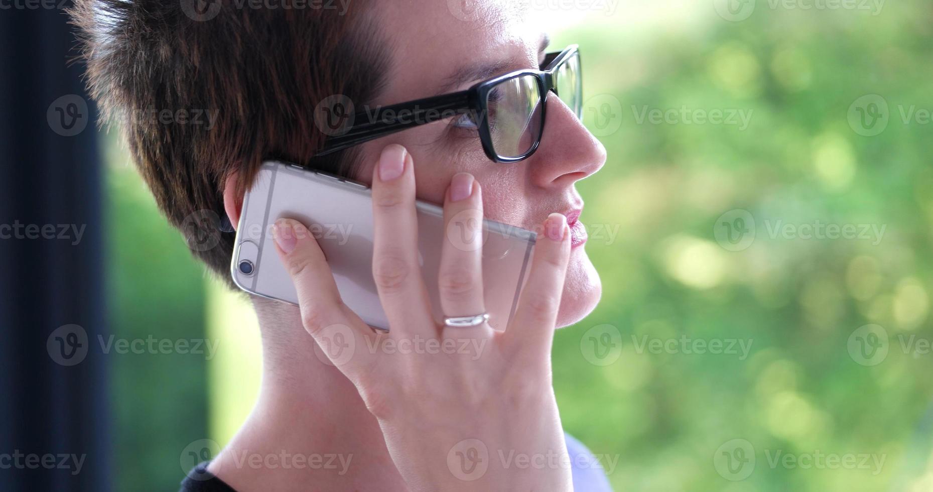 mujer elegante usando teléfono móvil por ventana en edificio de oficinas foto