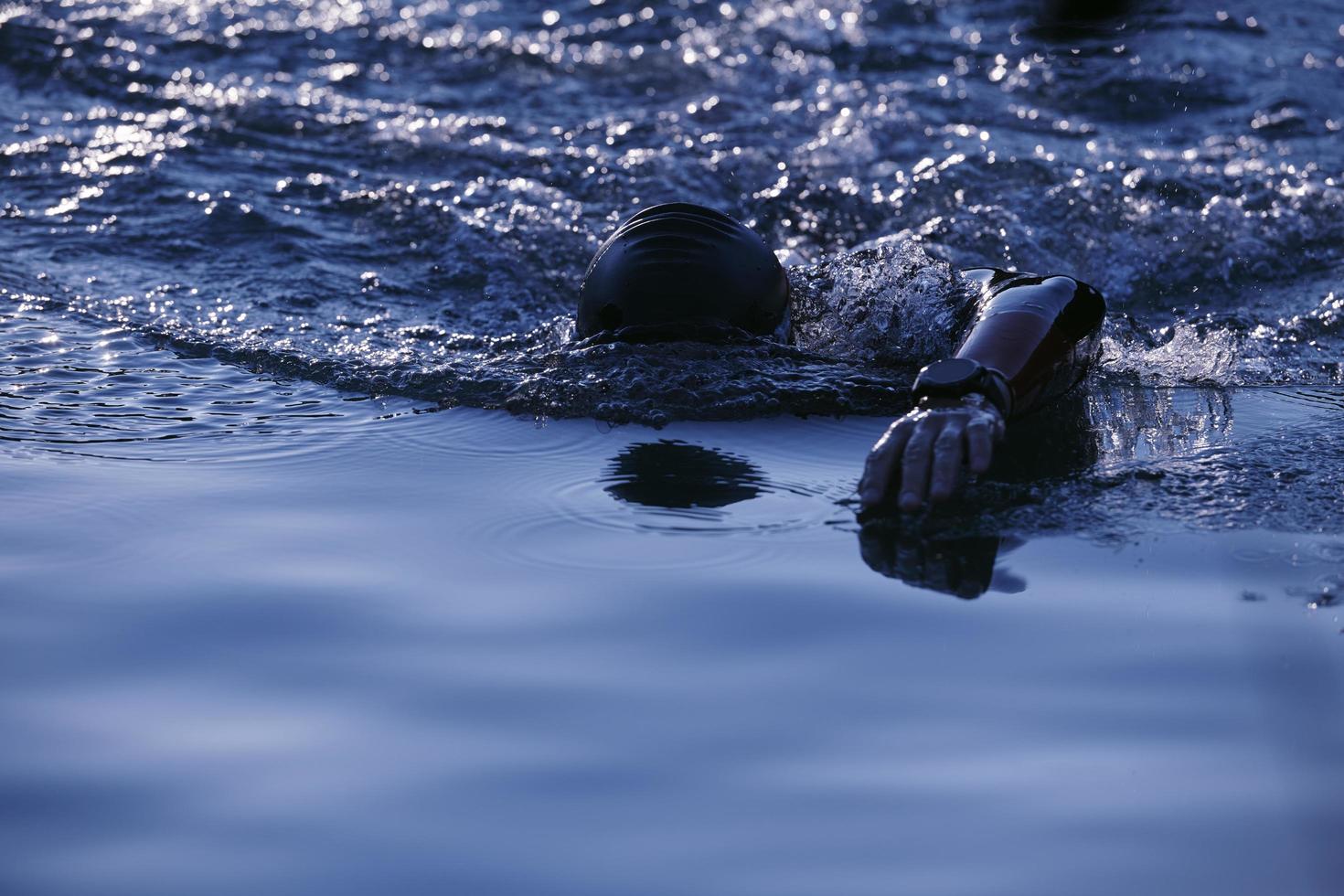 atleta de triatlón nadando en el lago al amanecer usando traje de neopreno foto