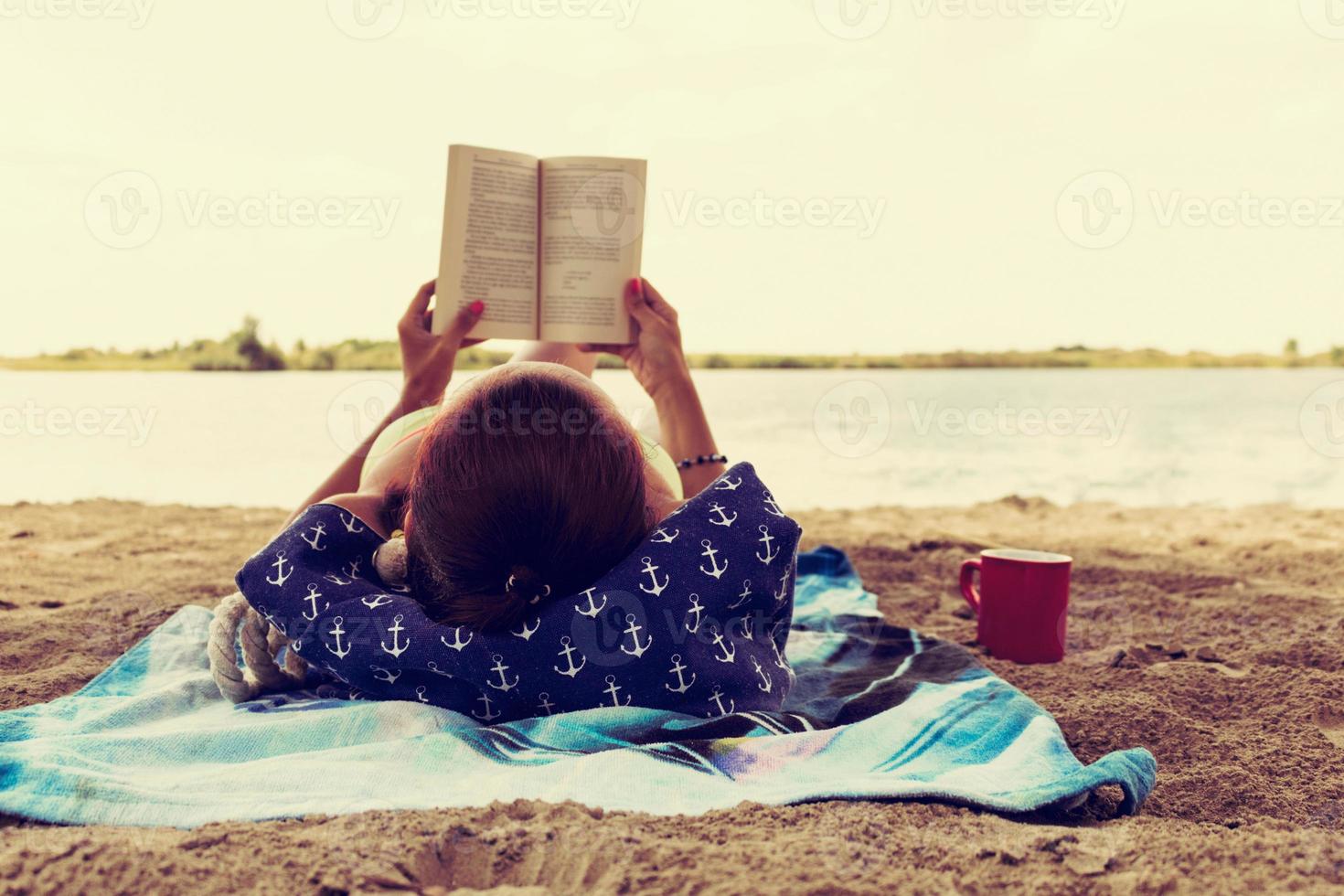 Relaxed woman reading book on sandy beach during summer vacation. photo