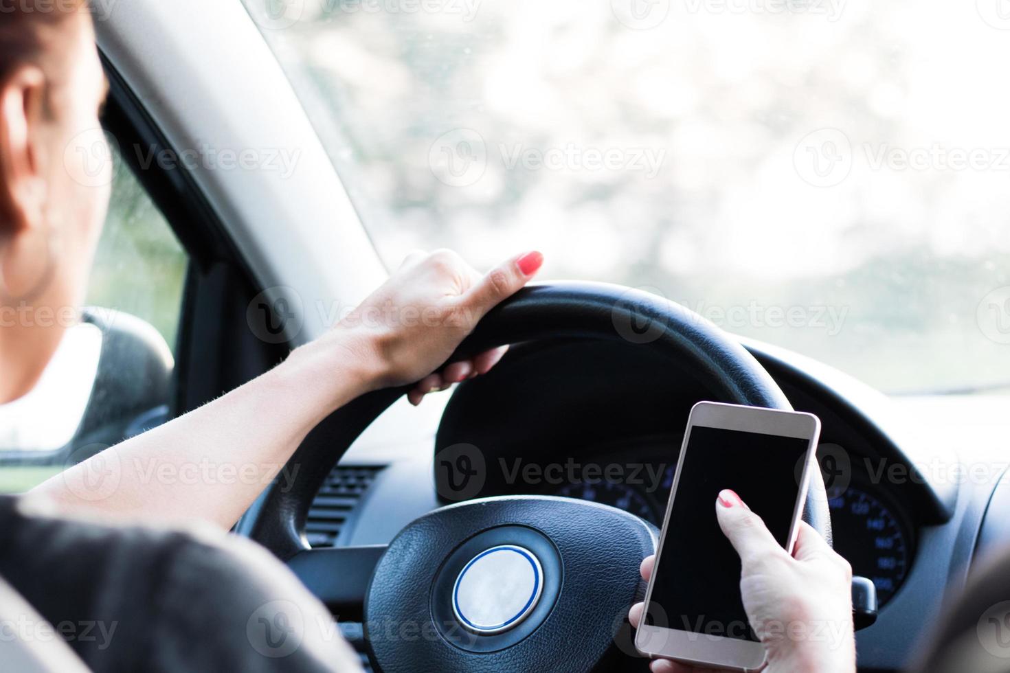 primer plano de una mujer conduciendo un coche y enviando mensajes de texto por teléfono móvil. foto