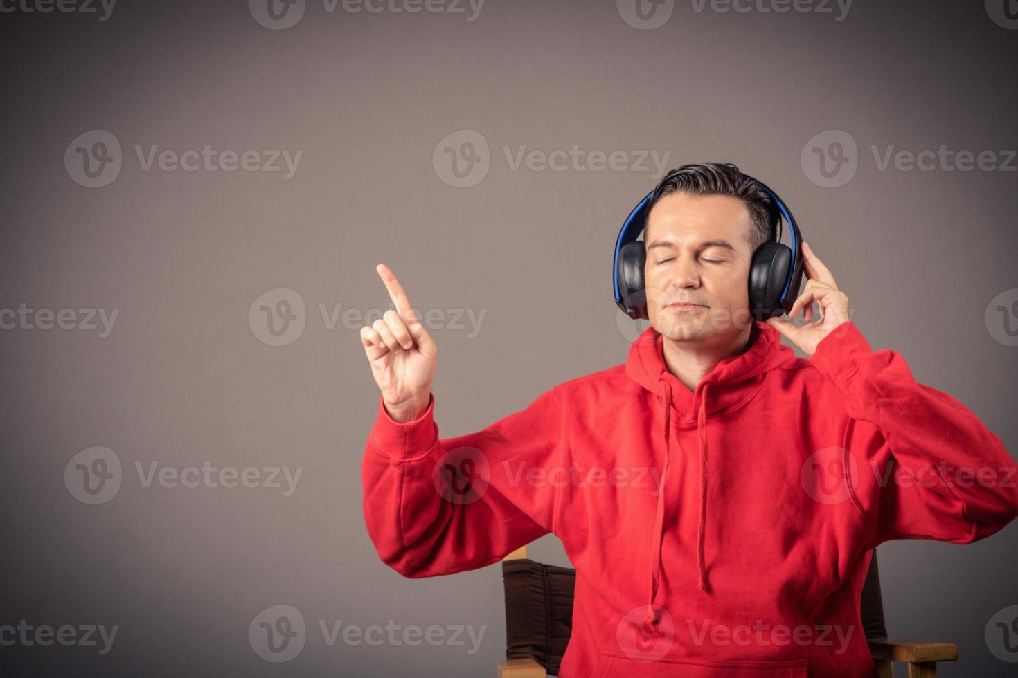 Portrait of man with headphones listening music with eyes closed and pointing at copy space on wall. photo